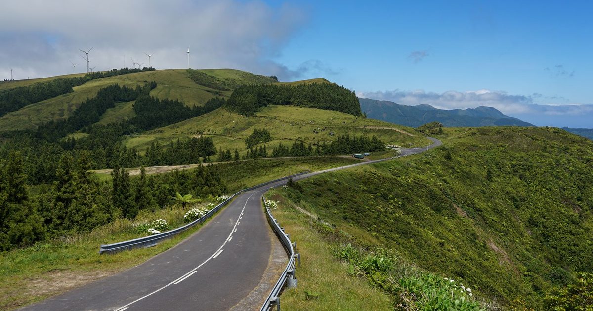 A winding road through green hills with wind turbines