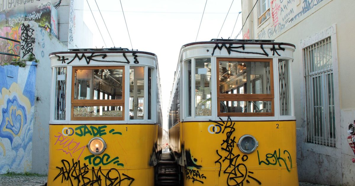 Two yellow trams on a graffiti-covered street in Lisbon, Portugal