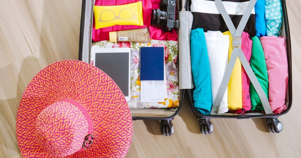 A suitcase packed with clothes, a camera and a sun hat